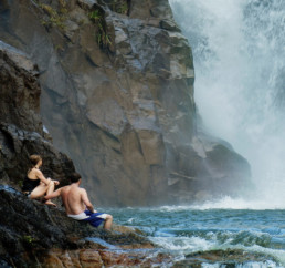 Pareja sentada en rocas a la orilla de una cascada en Mountain Pine Ridge Belice